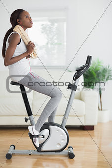 Black woman on an exercise bike holding a towel
