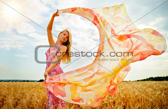 The young woman in the field holding scarf to wind.