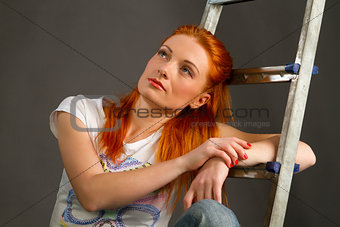 Beautiful young red-haired girl leaning on a ladder