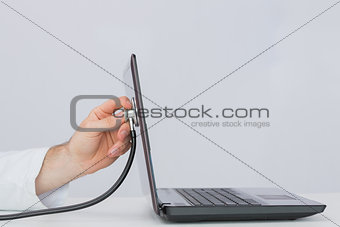 Hand examining laptop with stethoscope