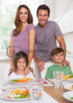 Two children and their parents smiling at the camera at dinner table