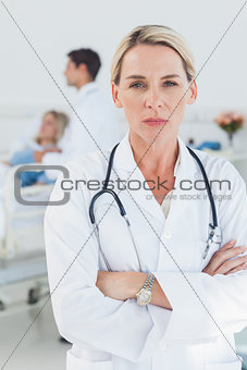 Serious doctor posing with doctor attending patient on background