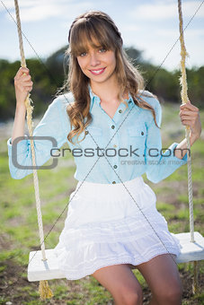 Smiling young model relaxing sitting on swing
