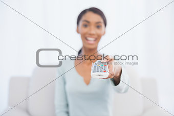 Cheerful pretty woman sitting on sofa changing tv channel