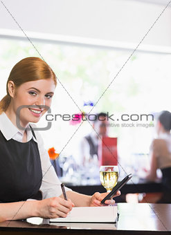 Smiling businesswoman writing and holding phone while looking at camera