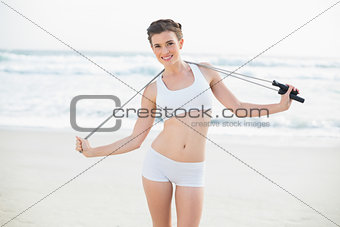 Pleased slim brown haired model in white sportswear holding a skipping rope