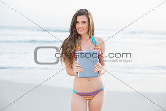 Cute slim brown haired model in coloured bikini holding a tablet pc