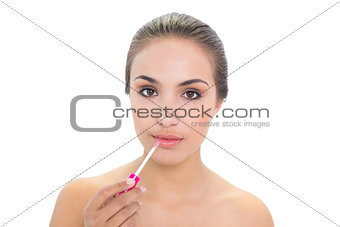 Content young brunette woman applying lip gloss