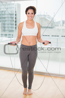 Sporty smiling brunette exercising with skipping rope