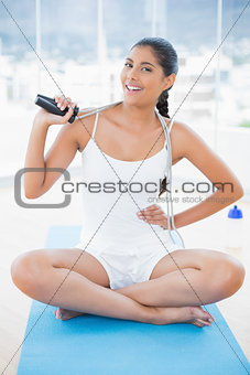 Smiling toned brunette sitting on floor with skipping rope