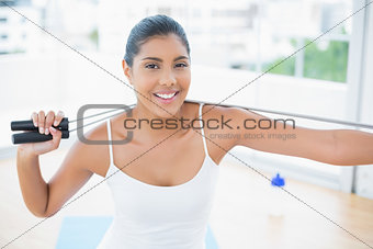 Happy toned brunette sitting on floor with skipping rope