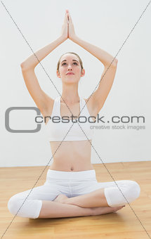 Attractive blonde woman sitting in lotus position raising her hands