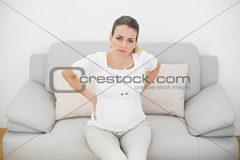 Lovely pregnant woman touching her injured back looking seriously at camera