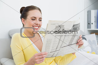 Smiling woman reading newspaper on sofa at home