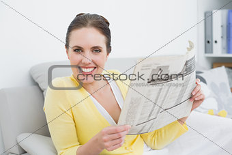 Portrait of a smiling woman reading newspaper at home