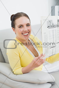 Smiling woman reading newspaper at home