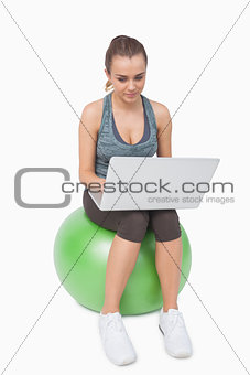Fit woman using her notebook sitting on balance ball