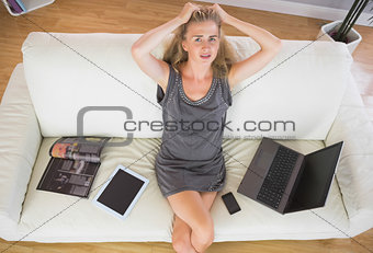 Casual frustrated blonde relaxing on couch next to several electronic devices