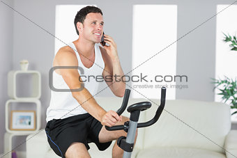 Smiling sporty man exercising on bike and phoning