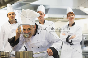 Head chef tasting a soup and smiling at camera