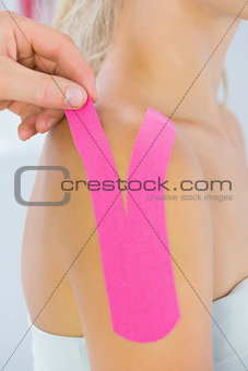 Physiotherapist putting on kinesio tape on female patients shoulder