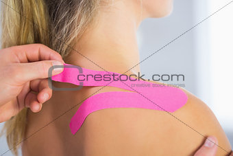 Physiotherapist applying kinesio tape on female patients shoulder