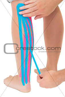 Physiotherapist applying pink and blue kinesio tape on patients leg