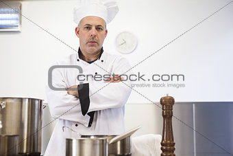 Serious head chef standing arms crossed behind pot