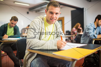 Smiling student with others writing notes in classroom