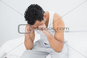 Young sleepy man rubbing his eyes on bed