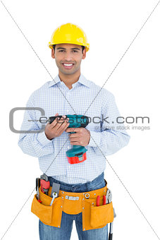 Smiling handsome young handyman in hard hat holding drill