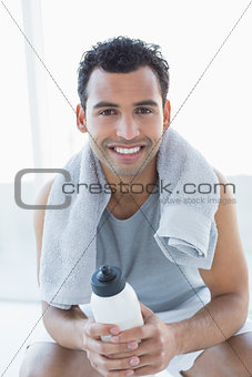 Man with towel around neck holding water bottle in fitness studio