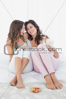 Female friends sitting on bed with arm around