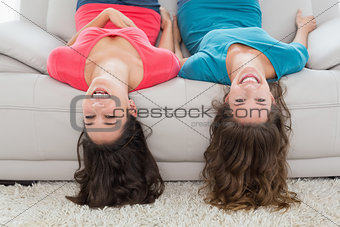 Female friends lying upside down on sofa at home