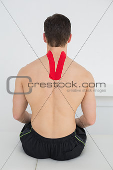 Rear view of a shirtless man with kinesio tape on back