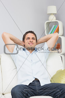 Thoughtful man sitting with hands behind head in the living room