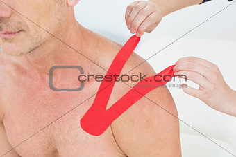 Hands putting on red kinesio tape on patient's shoulder