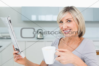 Smiling woman with coffee cup and newspaper in kitchen