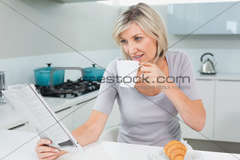 Woman drinking coffee while reading newspaper in kitchen