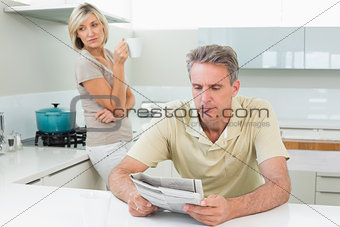 Man reading newspaper while woman at kitchen