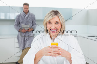 Woman with orange and man reading newspaper in kitchen