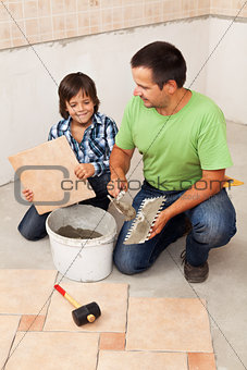 Man laying ceramic floor tiles helped by small boy