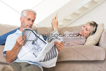 Couple with newspaper and cellphone in living room at home