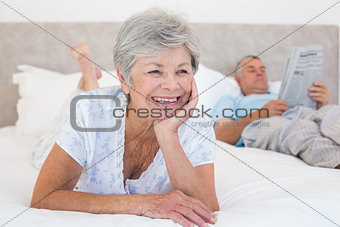 Senior woman with man reading newspaper on bed