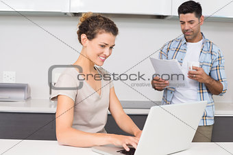 Pretty woman using laptop while partner reads the newspaper