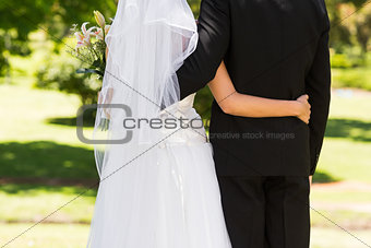 Mid section of a newlywed with arms around in park