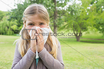 Girl blowing nose with tissue paper at park