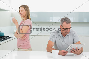 Displeased woman drinking coffee while man reading newspaper in kitchen