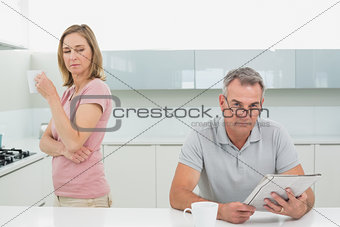Woman drinking coffee while man reading newspaper in kitchen