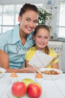 Woman with daughter reading greeting card at breakfast table